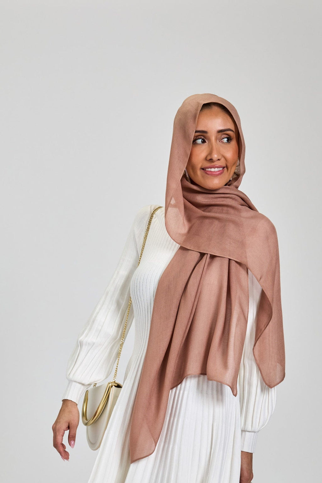 Woman wearing a white pleated dress and dusty rose hijab on a white background
